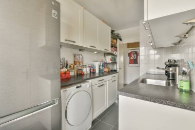 Amsterdam, Hollanda - 10 Nisan 2021: Görüntünün merkezinde beyaz dolapları ve siyah tezgahları olan bir mutfak bir çamaşır makinesi, bulaşıkçı, kuru temizlemecidir.