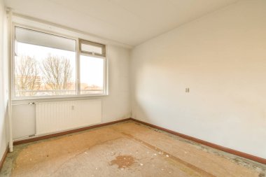 Ahşap döşemesi ve duvarlarında beyaz boya olan boş bir oda. Köşesinde bir pencere var.