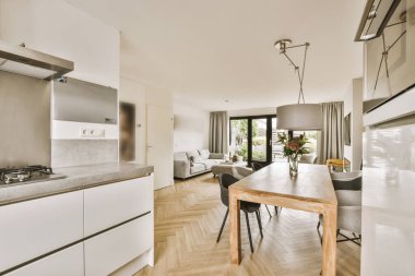 Beyaz duvarları, ahşap döşemeleri ve verandaya açılan açık kapısı olan bir evde mutfak ve yemek odası.