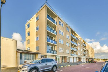 Yolun kenarına park etmiş bir araba çok katlı bir apartmanın önünde, camları ve balla kaplı.