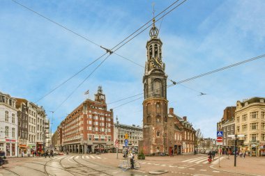 Bir kavşağın ortasında bir saat kulesi ve yanında yürüyen insanlar.,