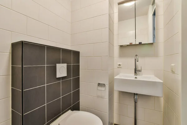 a bathroom with black and white tiles on the wall, sink and toilet in the photo is taken to the right