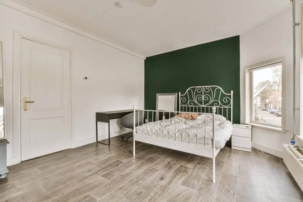 房间中央有一个有绿色墙壁和木制地板的卧室 有一个白色的金属床 — 图库照片