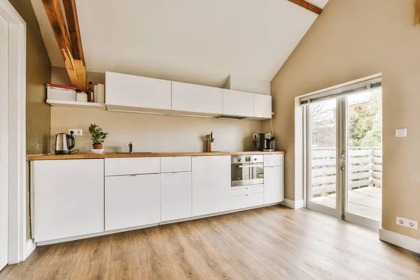 stock image a kitchen area with wood flooring and white cupboards on the walls, doors open to an outdoor patio