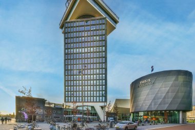 Amsterdam, Hollanda - 10 Nisan 2021: yanında saat olan büyük bir bina ve insanlar fotoğraf çekmek için sokakta dolaşıyorlar.