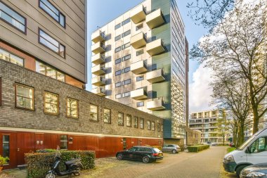 Amsterdam, Hollanda - 10 Nisan 2021: bazı arabalar arka planda binalar ve kaldırımda sıra sıra bekleyen ağaçlarla bir caddenin kenarına park edilmiş.