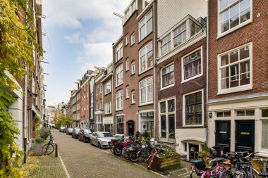 Bir şehir merkezinde caddenin kenarına park etmiş bazı bisikletlerin her tarafında binalar ve bitkiler var.