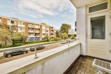 Arabaları kaldırıma park etmiş, binalar arka planda, ön kapıdan dışarı çıkarılmış.