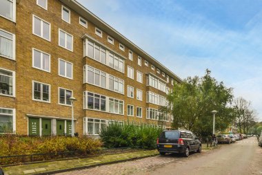 Amsterdam, Hollanda - 10 Nisan 2021: Kenarında arabalar park edilmiş bir şehir caddesi ve apartmanların önünde yol boyunca uzanan ağaçlar,