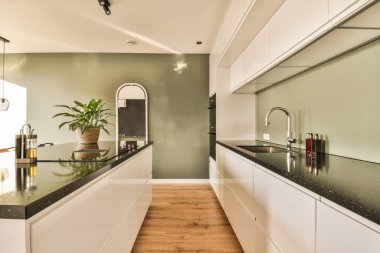 Beyaz dolapları ve siyah tezgahları olan modern bir mutfak. Odanın ortasında ahşap döşemeler var.