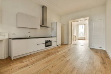 Boş bir mutfak, ahşap döşeme ve kapının iki tarafında da beyaz dolaplar var.