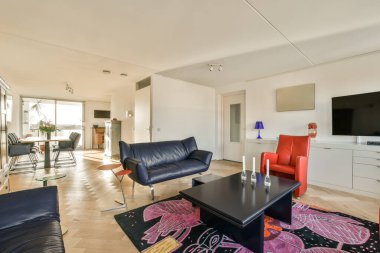 Oturma odası, mavi kanepeler ve yerde renkli halılar, bir televizyon seti.