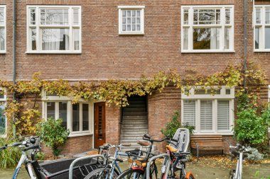 Amsterdam, Hollanda - 10 Nisan 2021: Binanın yan tarafında sarmaşıklar ve pencereler büyüyen bir evin önüne park edilmiş iki bisiklet