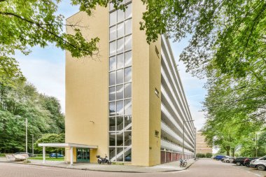 Amsterdam, Hollanda - 10 Nisan 2021: Otoparkın yanına park edilmiş bir ofis binası ve binanın her iki tarafında da ağaçlar var.