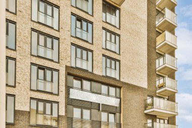 En üst katında birçok pencere ve balya olan bir apartmanın önünde beyaz bir gökyüzü var.