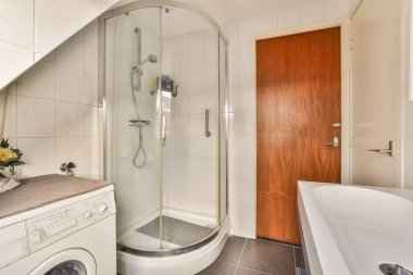 Lavabonun önündeki duş kabininin yanında çamaşır makinesi ve kurutma makinesi olan banyo beyazdır.