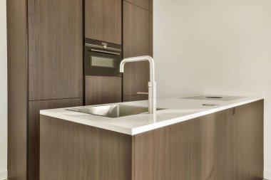 Beyaz tezgahlı modern bir mutfak ve fotoğrafta siyah ahşap dolaplar ön taraftan çekiliyor, lavaboyu gösteriyor.