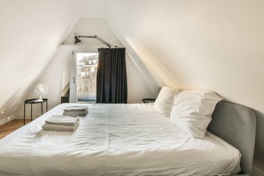 Odanın köşesinde beyaz duvarları ve odanın diğer tarafında ahşap döşemeleri olan bir yatak.