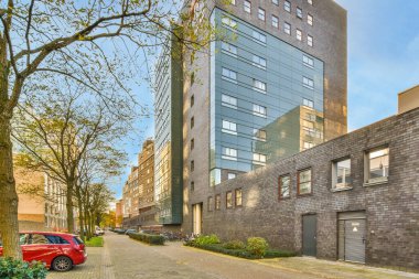 Amsterdam, Hollanda - 10 Nisan 2021: yan tarafında arabalar ve arka tarafında binalar olan bir şehir caddesi, yolun yanında bazı ağaçlar büyüyor