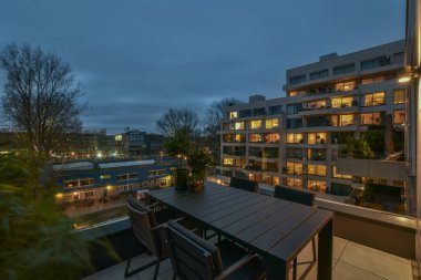 Amsterdam, Hollanda - 10 Nisan 2021: Geceleri ışıklar açık ve ağaçlar önde bir şehir - bir apartman balkonundan görüntü alındı