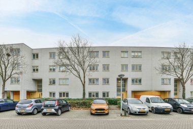 Amsterdam, Hollanda - 10 Nisan 2021: Güneşli bir günde bir apartmanın önüne park etmiş bazı arabalar ve üzerlerinde beyaz bulutlar var.
