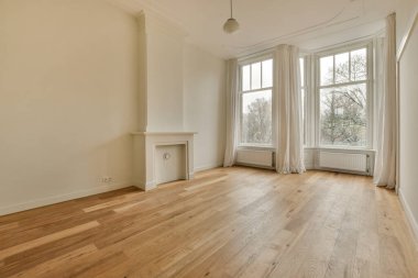 boş bir oturma odası ahşap döşeme ve geniş pencereli uzaktaki ağaçlara bakan beyaz perdeler