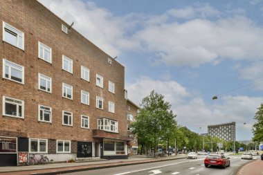 Amsterdam, Hollanda - 10 Nisan 2021: kırmızı tuğlalı bir apartmanın önünde yol kenarına park edilmiş arabalı bir şehir sokağı