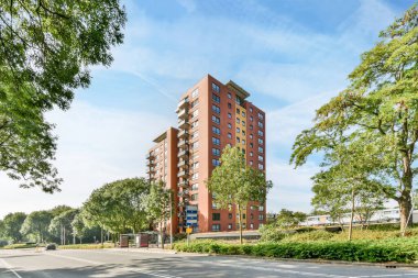 Amsterdam, Hollanda - 10 Nisan 2021: Ağaçların ve çalıların önünde, mavi gökyüzü arka planına sahip bir caddenin köşesinde bir apartman.