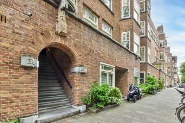 Amsterdam, Hollanda - 10 Nisan 2021: Hollanda, Amsterdam 'da kaldırıma parkedilmiş merdivenleri ve bisikleti olan tuğlalı bir bina