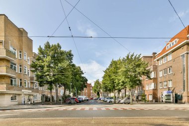 Amsterdam, Hollanda - 10 Nisan 2021: Yan tarafında arabalar ve arka tarafında evler olan boş bir cadde, gökyüzünde bazı binalar görülebilir.
