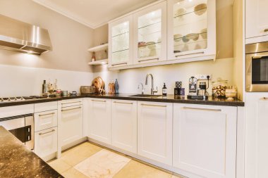 Bu fotoğrafta tezgahların üzerinde beyaz dolaplar ve siyah tezgahlar olan bir mutfak içeriden çekilmiş.