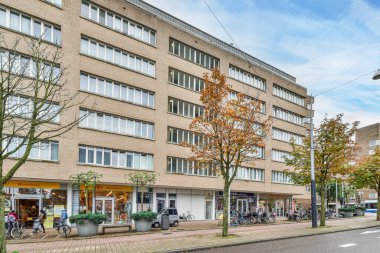 Amsterdam, Hollanda - 10 Nisan 2021: kaldırımlarda yürüyen insanlarla dolu bir şehir caddesi ve birçok penceresi olan bir apartmanın önünde park edilmiş arabalar.