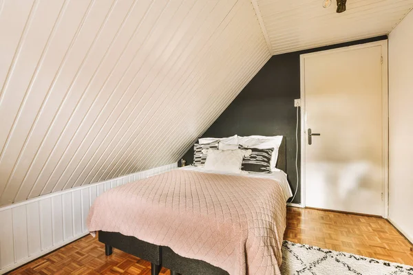 a bed in a room with white walls and wood flooring on the wall, there is a pink comforter