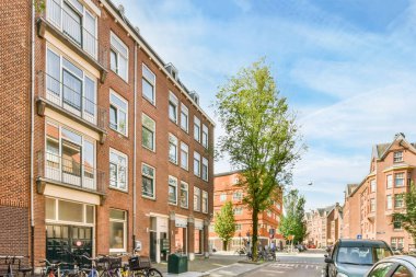 Amsterdam, Hollanda - 10 Nisan 2021: kaldırımlara park edilmiş bir şehir caddesi ve bazı binaların önünde yürüyen insanlar