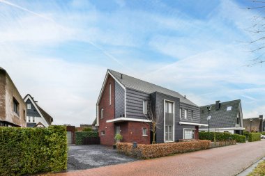 Amsterdam, Hollanda - 10 Nisan 2021: Ağaçların ve çalıların önündeki bazı evler, üzerlerinde mavi gökyüzü olan