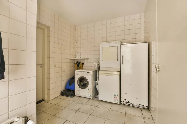 Un cuarto de lavado con azulejos blancos en las paredes y estantes de  madera frente a la lavadora secadora y secadora.