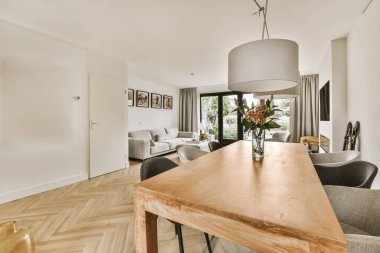 Ahşap döşemeli ve beyaz duvarlı bir oturma odası yemek masası, iki sandalye ve bir lamba.