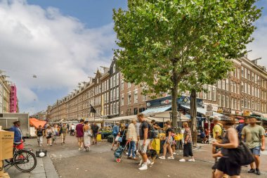 Amsterdam, Hollanda - 10 Nisan 2021: Güneşli bir günde bazı dükkanların ve binaların önünde yürüyen insanlar