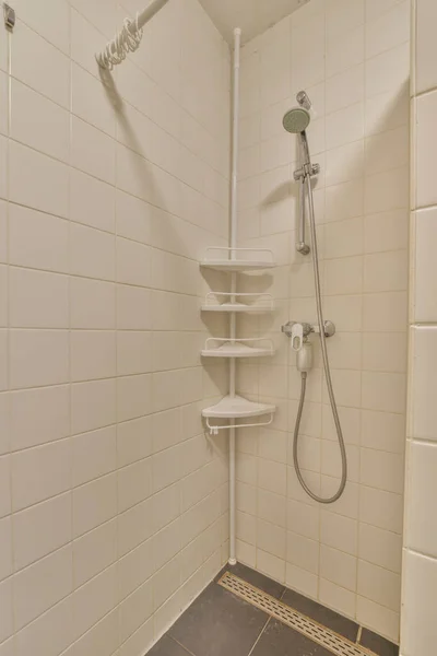 壁にタイル張りの床と白いタイルのシャワー室シャワーヘッドの上に棚があります — ストック写真