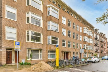 Bitişiğinde bisikletleri olan bir apartman ve binanın önüne park edilmiş arabalar.,