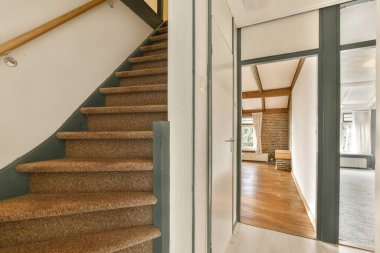 Ahşap zeminli bir evin içi ve başka bir odaya açılan açık bir kapıya çıkan merdiven.