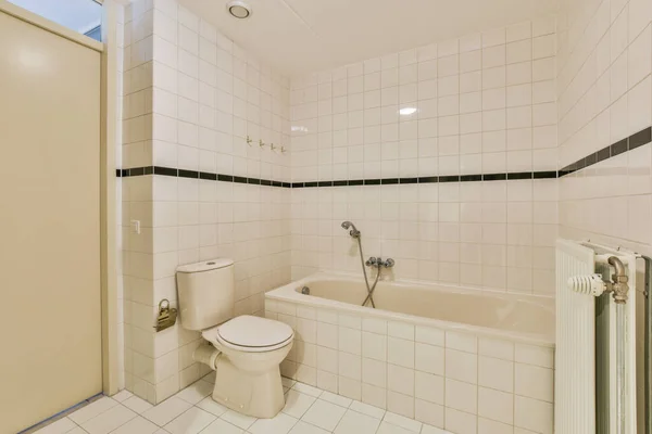 浴槽やトイレの周りに白いタイル張りの壁と黒いトリムのバスルームがあります — ストック写真