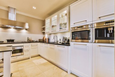 Resmin ortasında beyaz dolapları ve siyah tezgahları olan bir mutfak fırın, bulaşık makinesi, mikrodalga fırın ve tost makinesidir.