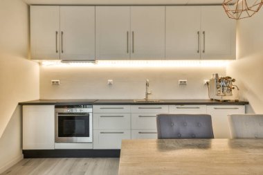 Lavabonun önünde beyaz dolapları ve siyah tezgahları olan bir mutfak bir fırın, mikrodalga fırın ve bulaşık makinesidir.