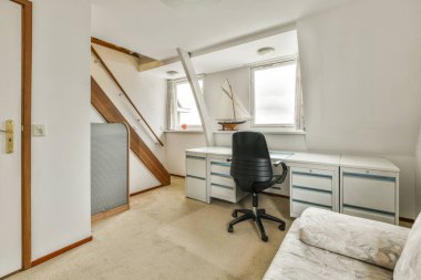 Masası, sandalyesi ve bilgisayarı olan bir oda başka bir odaya açılan açık bir kapının önünde.