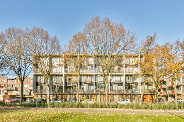 Amsterdam, Hollanda - 10 Nisan 2021: Ön planda ağaçlar ve caddelerde yan yana park edilmiş arabalar olan bir apartman kompleksi