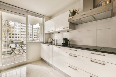 Beyaz dolapları ve siyah tezgahları olan bir mutfak. Açık hava avlusuna açılan cam kapının önünde.