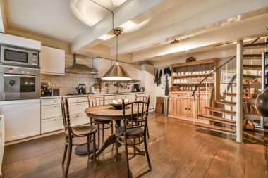 Ahşap zemin, beyaz dolaplar, ahşap döşemeler ve duvarda fırın olan bir evde mutfak ve yemek odası.