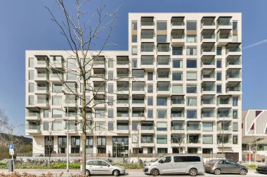 Amsterdam, Hollanda - 10 Nisan 2021: Arabaların olduğu bir apartman ve önünde bir ağaç var.