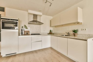 Tezgahın üstünde beyaz dolaplar ve aletlerle dolu bir mutfak. Ahşap döşemeleri olan açık bir alanda.